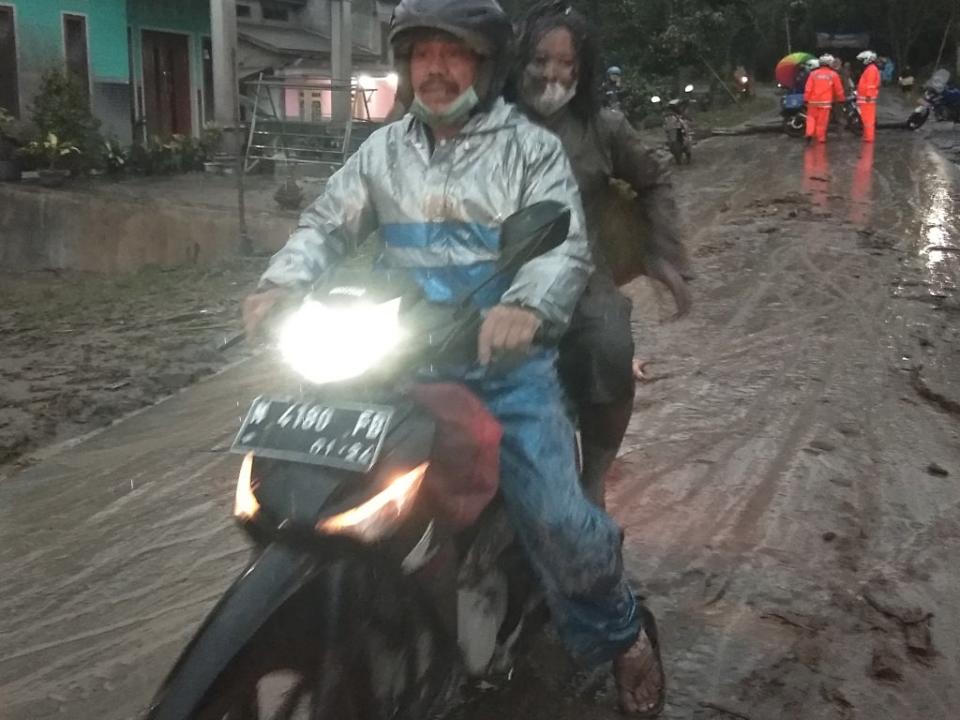 A pair ride a motorbike on a road covered with volcanic ash (Reuters)