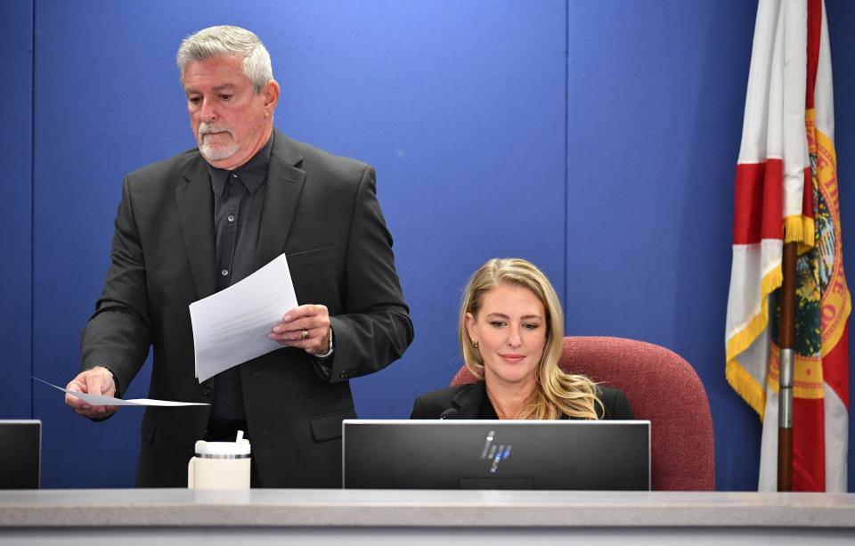 Sarasota County School Board member Tom Edwards, left, hands out a proposal for the board to consider writing a letter to Gov. Ron DeSantis, asking him to remove their colleague, Bridget Ziegler, right, during a meeting Tuesday evening, Dec. 12, 2023. The School Board approved a resolution calling on Ziegler to resign, but it has no authority to force her off the board.