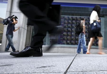 Passersby walk past an electronic stock quotation board outside a brokerage in Tokyo June 24, 2015. REUTERS/Issei Kato/Files