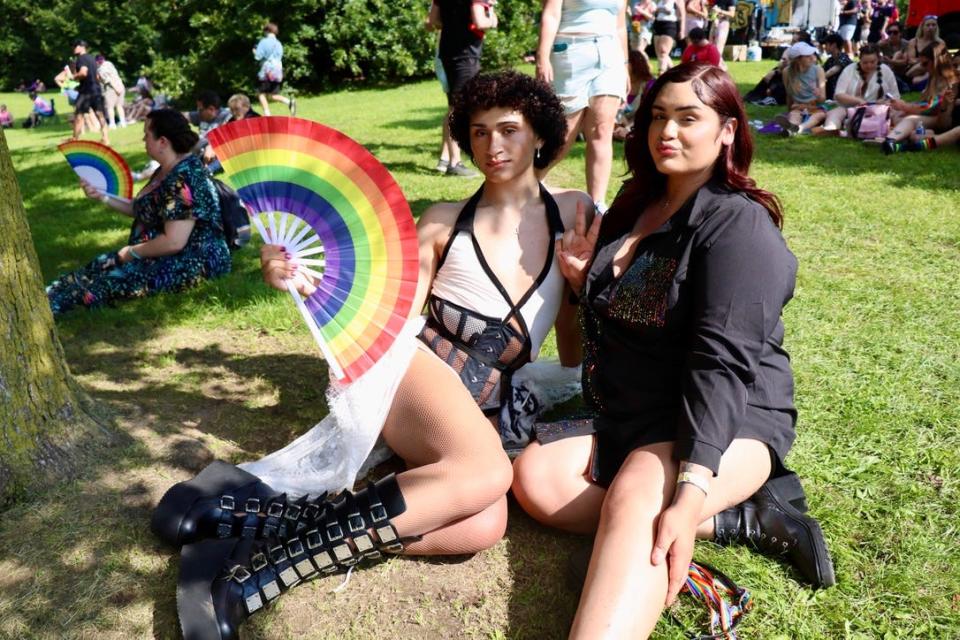 Cynn Cruz and Eli Alejandro lounge on a grassy hill near the main stage on the 2024 Rochester Pride Festival grounds.