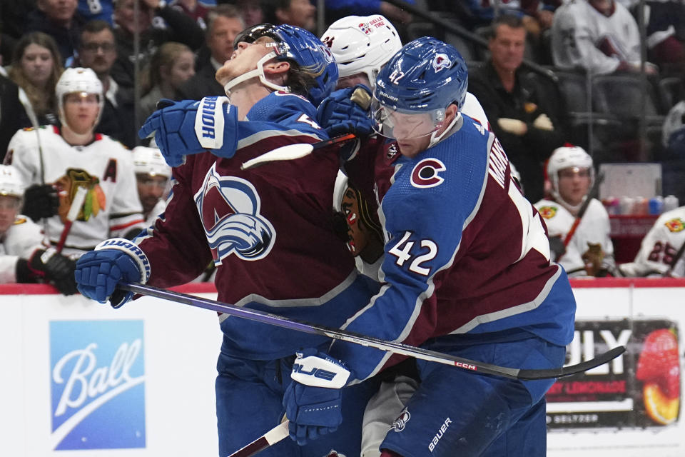Colorado Avalanche defenseman Bowen Byram (4) is hit from behind by Chicago Blackhawks center Sam Lafferty (24), next to Avalanche defenseman Josh Manson (42) during the second period of an NHL hockey game Wednesday, Oct. 12, 2022, in Denver. (AP Photo/Jack Dempsey)
