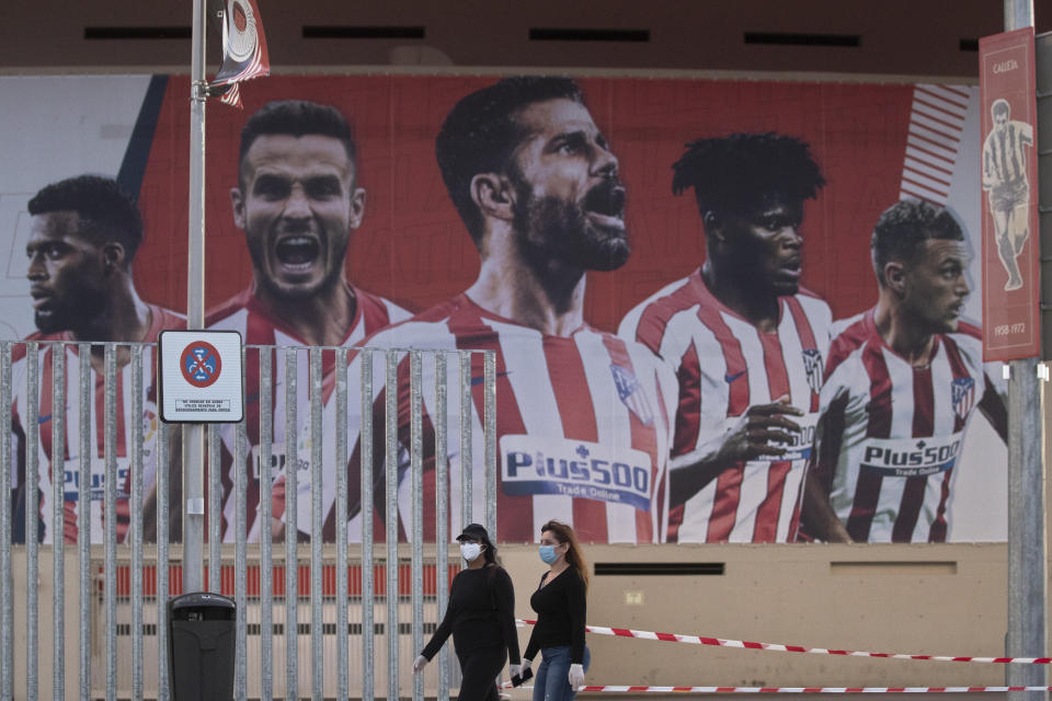 Dos mujeres con mascarillas pasan frente a un afiche gigante en el estadio del Atlético de Madrid, el martes 5 de mayo de 2020. (AP Foto/Paul White)