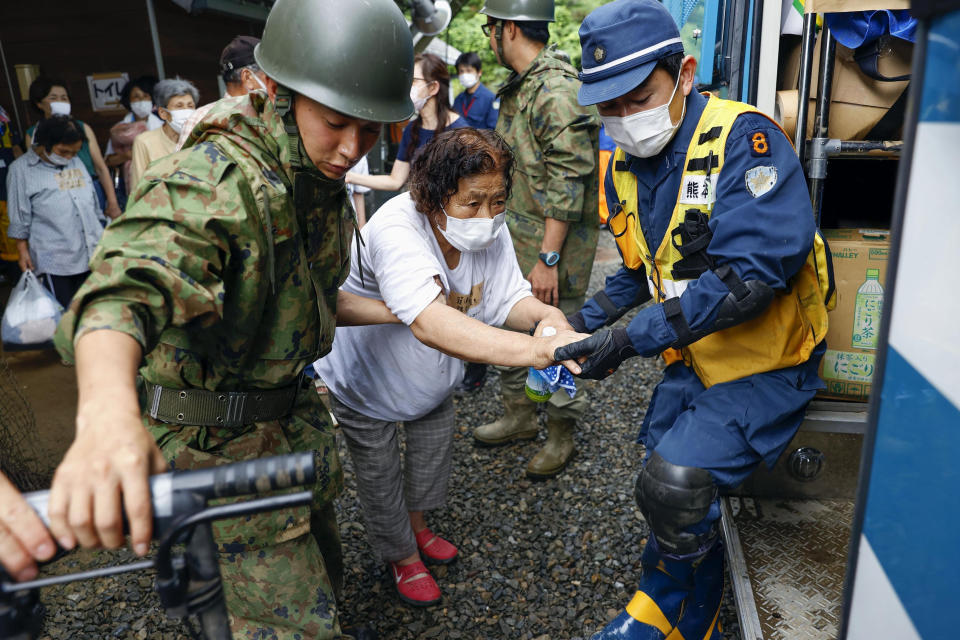 A woman is helped to get into a police vehicle to move from a shelter to another shelter in Kumamura, Kumamoto prefecture, southern Japan Monday, July 6, 2020. Rescue operations continued and rain threatened wider areas of the main island of Kyushu. (Kota Endo/Kyodo News via AP)