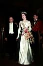 <p>The queen dons a satin sleeveless ball grown, chandelier earrings, and long satin gloves while carrying an elaborate bouquet with orchids and baby's breath.</p>