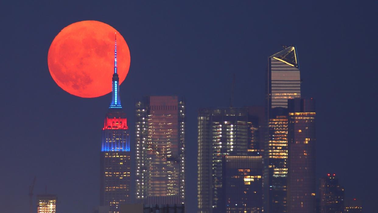  The full Buck Moon or Thunder Moon (a red full moon) passes behind Hudson Yards and the Empire State Building lit in the flag colors of countries competing in the Tokyo Olympics as it rises in New York City on July 23, 2021 as seen from Lyndhurst, New Jersey. 