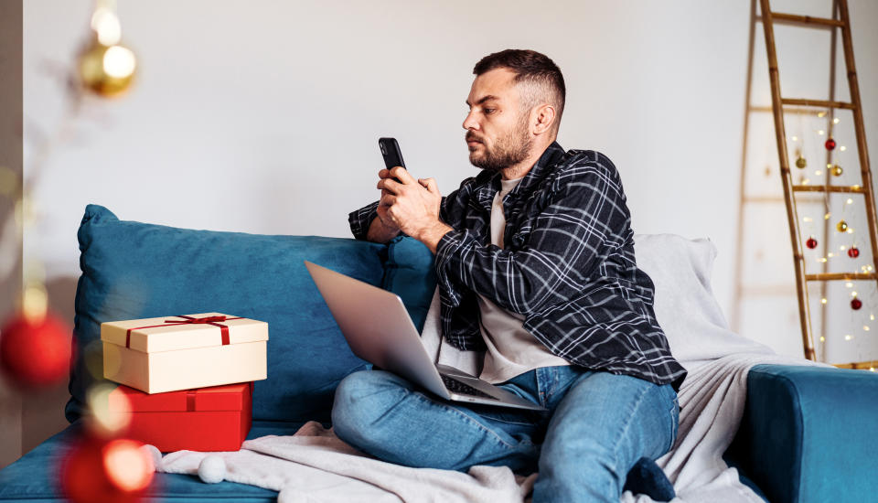man using his mobile phone messaging online while sitting on sofa at home during christmas holiday.