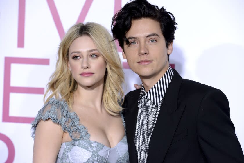 A blond woman in a blue dress posing with a man with dark hair in a black suit