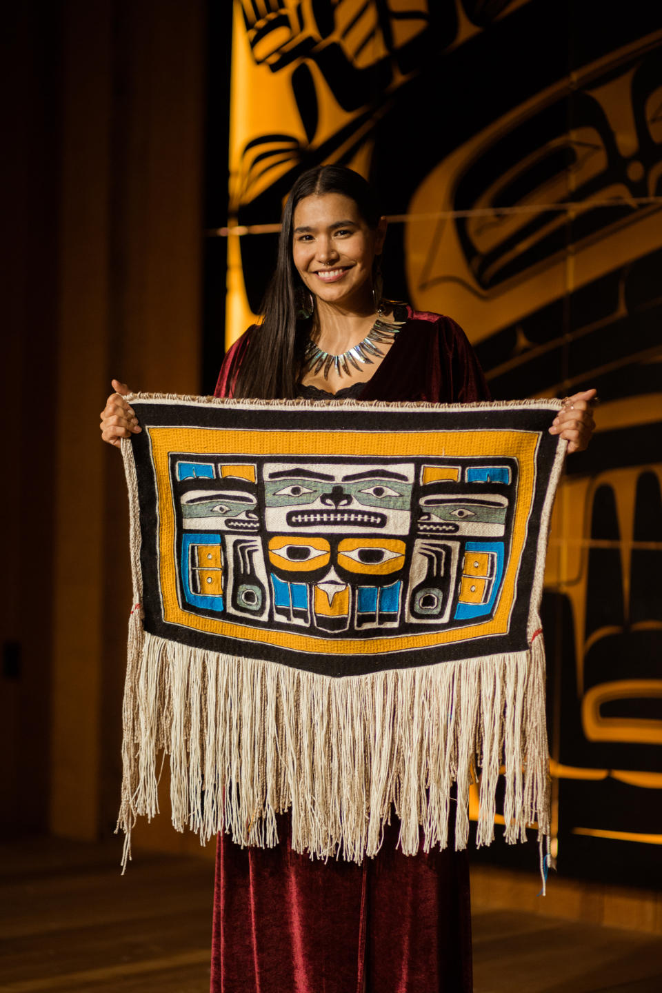 Jackson holds her Naax̲éin Chilkat robe titled “For The Stolen: A Journey Into Healing.” The Chilkat style features complex formline shapes woven in separate sections that are joined together to complete the final design, whereas Ravenstail designs are more geometric and twined as an entire piece using horizontal rows.