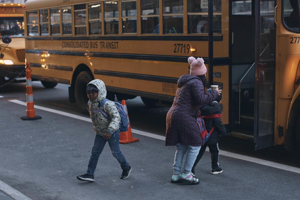 Migrant children take a school bus in front of the Row Hotel that serves as migrant shelter on Tuesday, Dec. 12, 2023, in New York. It could be a cold, grim New Year for thousands of migrant families living in New York City’s emergency shelter system. With winter setting in, they are being told they need to clear out, with no guarantee they’ll be given a bed elsewhere. (AP Photo/Andres Kudacki)