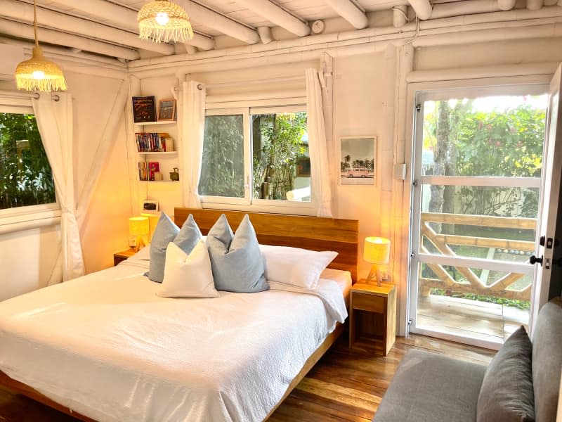 Wood bed under window in white bamboo and wood bedroom with matching table and pendant lamps.