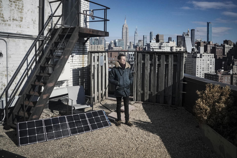Josh Spodek stands facing the sun for "some vitamin D" after setting up a portable solar on the rooftop of his co-op apartment building to charge his phone and laptop, Tuesday Jan. 24, 2023, in New York. Spodek is living grid-free in his Greenwich Village apartment after a decision to go packaging-free. "My goal was a month and I didn't anticipate I'd make it more than a few days," said Spodek. "I am in month nine now." (AP Photo/Bebeto Matthews)