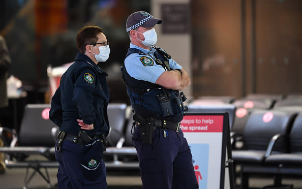 Police officers wear face masks as they watch passengers arrive from a Qantas flight at Sydney Airport on one of the last flights out of Melbourne to Sydney.