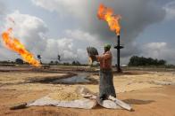 A woman empties a plastic bowl filled with tapioca close to a gas flaring furnace in Ughelli, Delta State