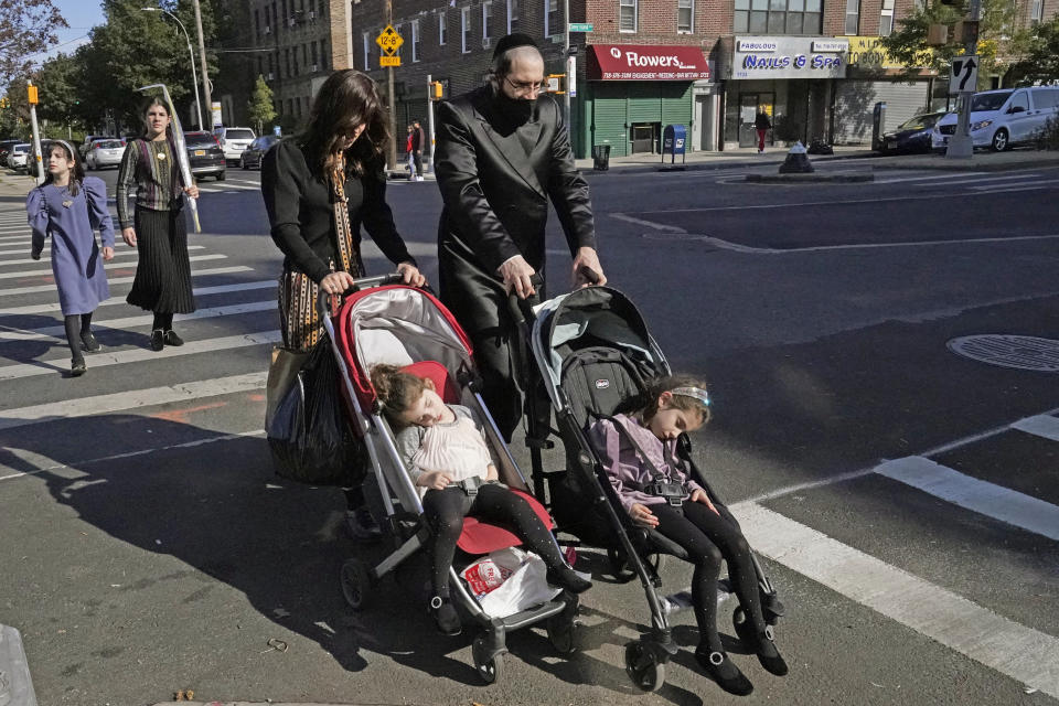 An ultra-Orthodox Jewish man and woman wheel strollers with sleeping children in them as they cross a street on the Jewish joldiay of Sukkot, Sunday, Oct. 4, 2020, in the Borough Park neighborhood of Brooklyn in New York. New York City's mayor said Sunday that he has asked the state for permission to close schools and reinstate restrictions on nonessential businesses in several neighborhoods, including Borough Park, because of a resurgence of the coronavirus. (AP Photo/Kathy Willens)