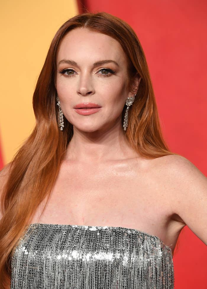 A closeup of Lindsay in a sequined strapless outfit with long earrings, posing at an event