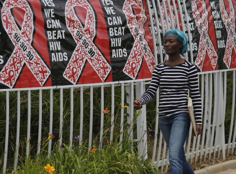 FILE - In this Friday, Dec. 1, 2017 file photo, a woman walks past a World AIDS Day banner in Johannesburg, South Africa. In 2019 fewer people in many parts of sub-Saharan Africa are dying of AIDS as treatment becomes more widely available, yet some officials worry that success may be encouraging a sense of complacency. (AP Photo/Denis Farrell, File)