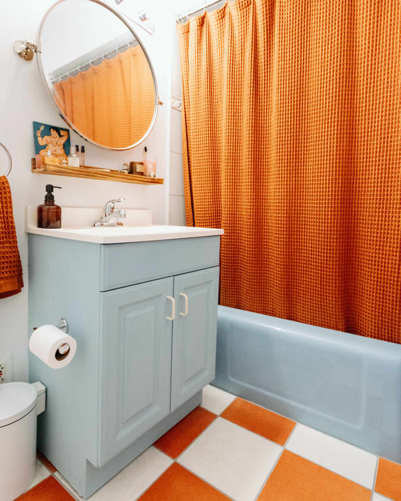 white bathroom with orange and white floor, pale blue tub, and orange shower curtain after makeover