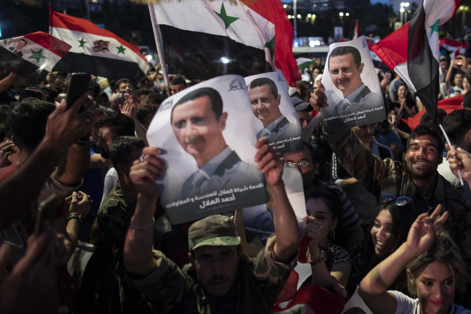 Syrian President Bashar Assad supporters hold up national flags and pictures of Assad as they celebrate at Omayyad Square, in Damascus, Syria, Thursday, May 27, 2021. (AP Photo/Hassan Ammar)