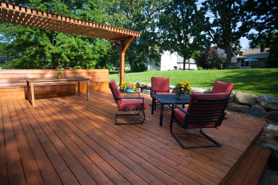 Deck with red patio furniture and pergola covering a picnic table. 