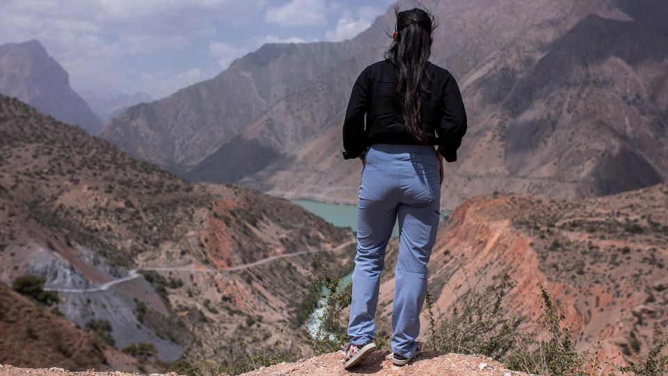 A woman stands on a ridge overlooking a mountain valley, facing away from the camera and wearing a pair of Patagonia Women’s Chambeau Rock Pants.