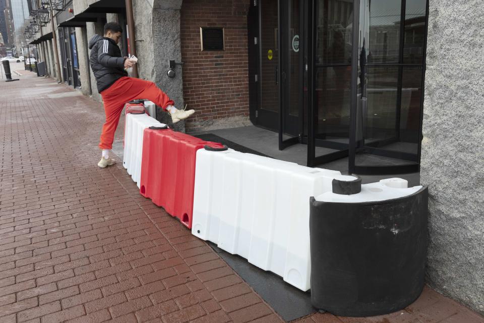 A man steps over a flood barrier at the entrance to a building on Long Wharf, Friday, Jan. 28, 2022, in Boston. Residents and officials in the Northeast and mid-Atlantic regions of the U.S. are bracing for a powerful winter storm expected to produce blizzard conditions Friday and Saturday. (AP Photo/Michael Dwyer)