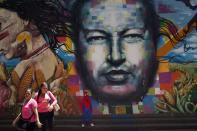 Un niño vestido con un disfraz de hombre araña posa para una foto junto a un mural del fallecido presidente de Venezuela, Hugo Chávez, pintado en una pared del Museo de Bellas Artes de Caracas, Venezuela, el martes 4 de marzo de 2014. Chávez murió hace un año pero su rostro y voz aparecen por doquier. La radio estatal usa su voz cuando cantaba el himno nacional cada mañana y la Guardia Nacional incluso le ha distorsionado su voz y la ha usado para diseminar a los manifestantes que arrojan piedras en la calle. (AP Foto/Rodrigo Abd)