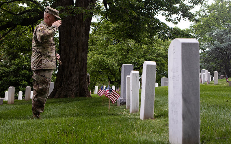 An Army soldier salutes as American flags are placed in front of headstones