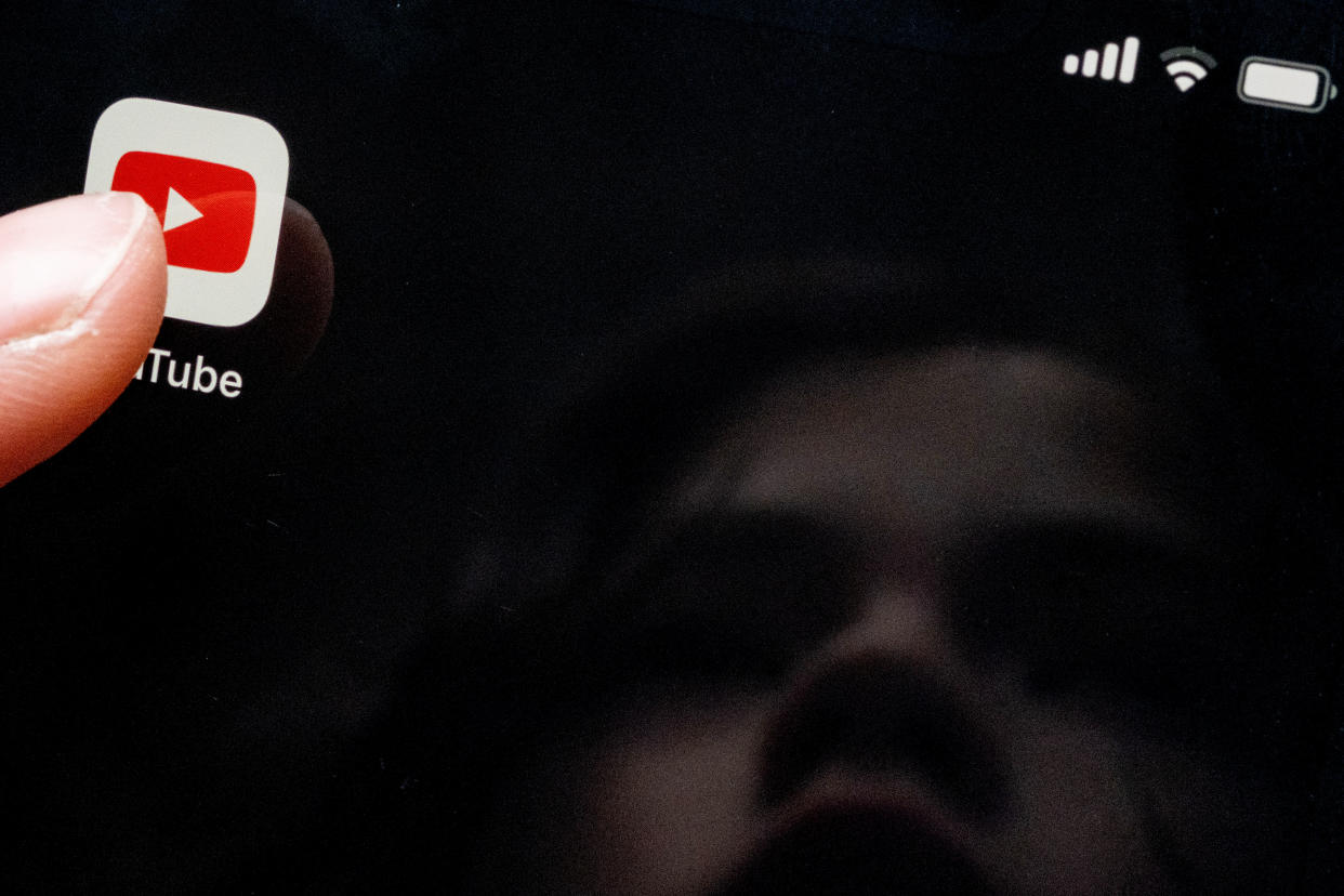 A child's face is reflected in a smartphone screen showing a YouTube app. 