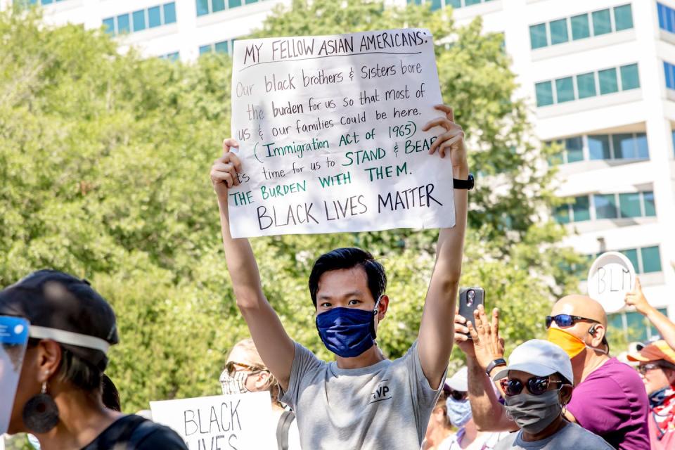 A young Asian man at a protest with a sign that says 'Black Lives Matter.'