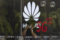 A worker wearing a mask to curb the spread of the coronavirus speaks on the phone near the Huawei logo in a store in Beijing on Wednesday, July 15, 2020. China's government accused Britain on Wednesday of colluding with Washington to hurt Chinese companies after tech giant Huawei was blocked from working on a next-generation mobile phone network. (AP Photo/Ng Han Guan)