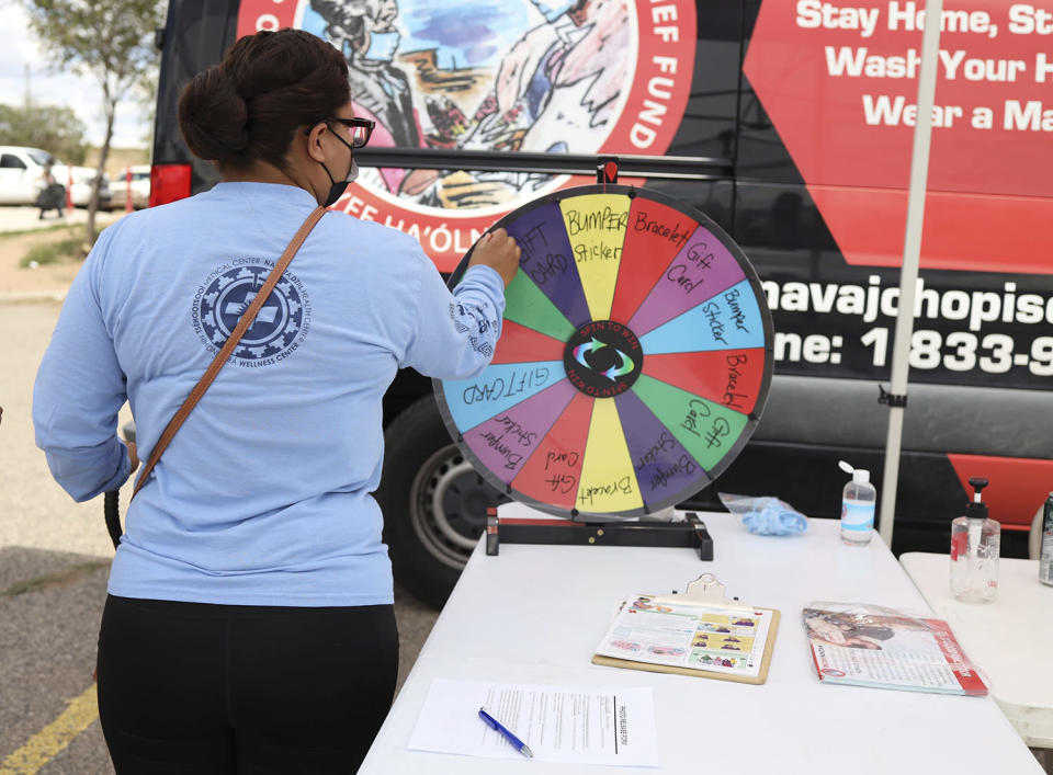In this photo provided by The Navajo & Hopi Families COVID-19 Relief Fund, a campaign participant spins the prize wheel after showing she was fully vaccinated at the Window Rock Flea Market in Window Rock, Ariz., on Aug. 21, 2021. Arizona is the only state where rural vaccine rates outpaced more populated counties according to a recent report from the U.S. Centers for Disease Control and Prevention. Public health experts believe the unexpected trend was mainly fueled by a group that lost a disproportionate number of lives to COVID-19: Native Americans. (Mihio Manus/The Navajo & Hopi Families COVID-19 Relief Fund via AP)