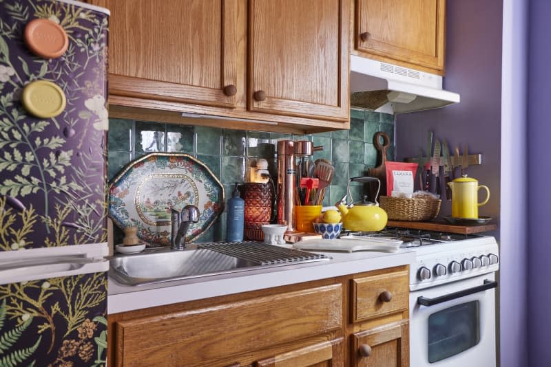 Colorful water kettle on kitchen stove in apartment kitchen with green tile backsplash.