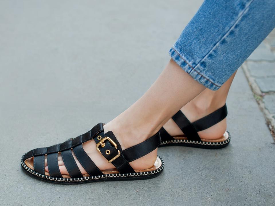 close up shot of someone wearing black fisherman sandals with a pair of light jeans