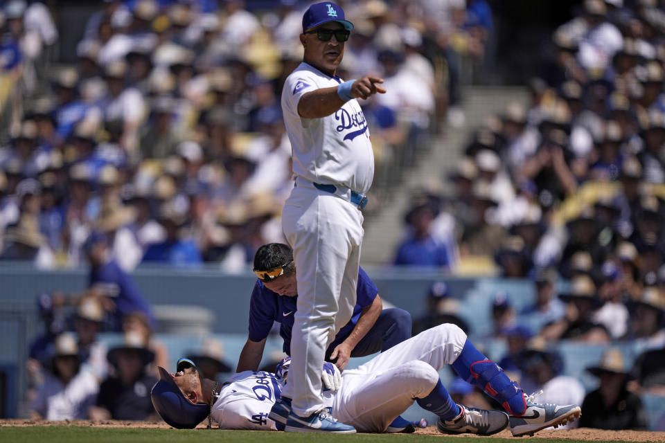 Los Angeles Dodgers' Mookie Betts, left, writhes on the ground after being hit by a pitch as manager Dave Roberts calls for a pinch runner and a trainer tends to him during the seventh inning of a baseball game against the Kansas City Royals Sunday, June 16, 2024, in Los Angeles. (AP Photo/Mark J. Terrill)