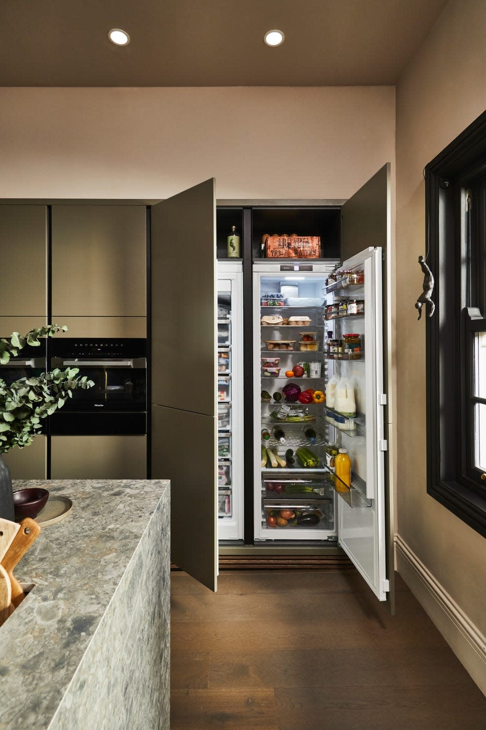 Open refrigerator in kitchen with grey stone island and dark wood floors