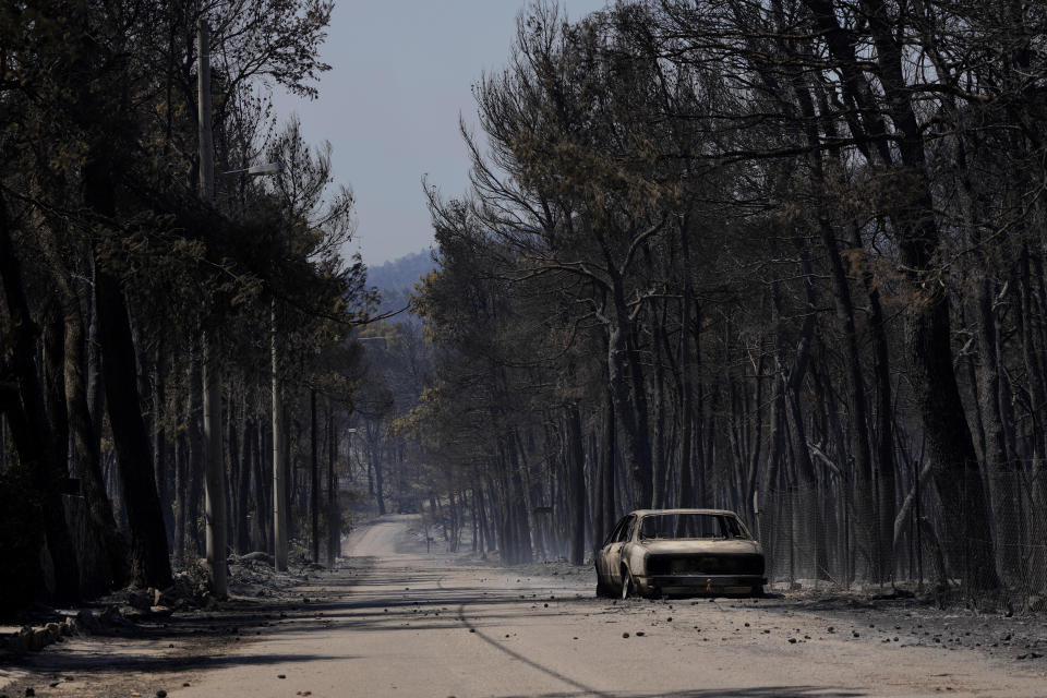 A burn car is seen at a road during a wildfire at Ipokratios Politia, in northern Athens, Greece, Saturday, Aug. 7, 2021. Wildfires rampaged through massive swathes of Greece's last remaining forests for yet another day Saturday, encroaching on inhabited areas and burning scores of homes, businesses and farmland. (AP Photo/Petros Karadjias)