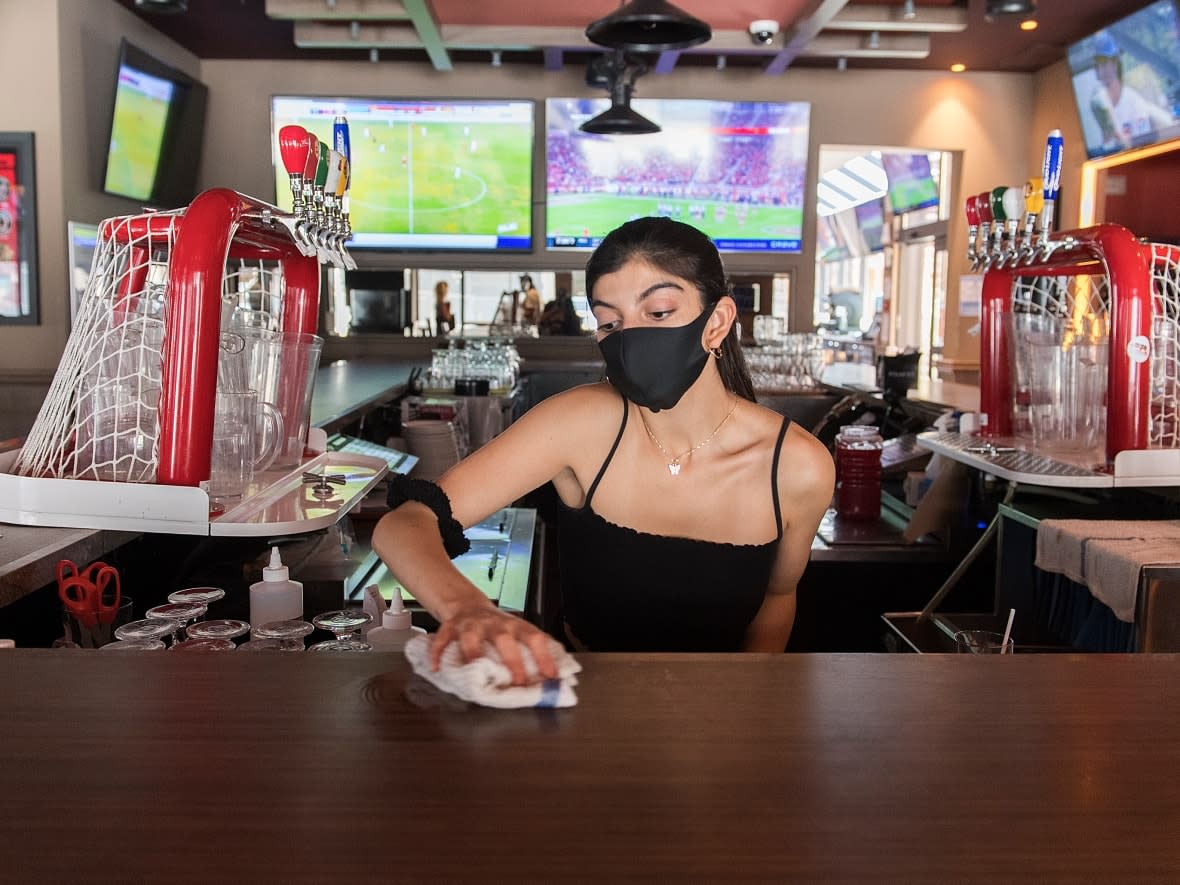 Canadians are used to tipping bartenders and servers, but some private liquor stores also have a gratuity option for customers to tip their staff while purchasing alcohol. Here, a server wipes down the counter at Station Sports bar in Montreal on July 25, 2020. (Graham Hughes/The Canadian Press - image credit)