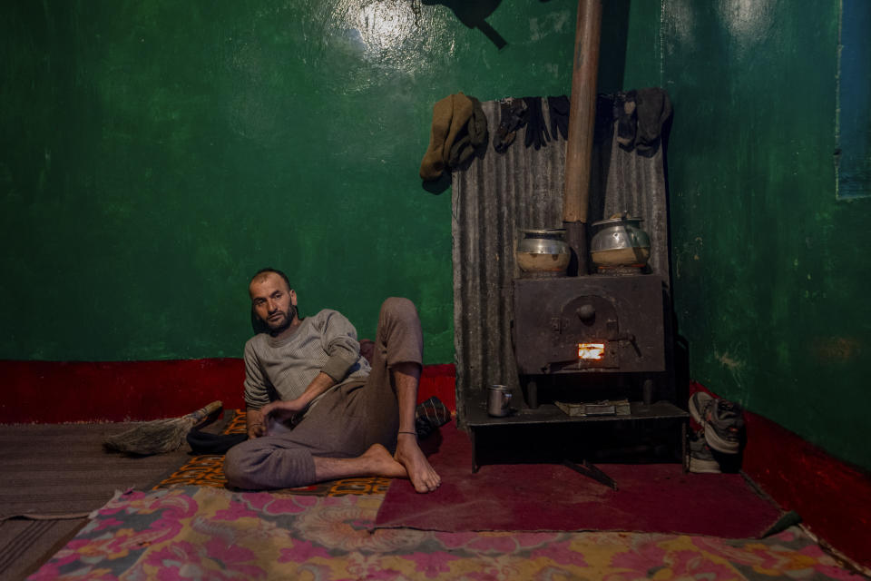 Kashmiri villager Mohammad Qayoom, who works as an army porter, warms himself sitting near a wood fire stove while cooking dinner in Drang village northwest of Srinagar, Indian controlled Kashmir Thursday, Dec. 21, 2023. Wood-fired stoves are commonly used in villages because they are not only utilized for cooking but also help in keeping the house warm. (AP Photo/Dar Yasin)