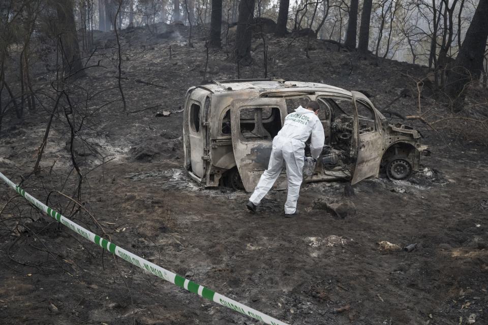 FILE - A police scientist inspects the remains of the car where two women died after a wildfire in Pontevedra, in the northwestern Spanish region of Galicia, Spain, Monday, Oct. 16, 2017. Wildfires in central Portugal killed more than 100 people in 2017. (AP Photo/Lalo R. Villar)