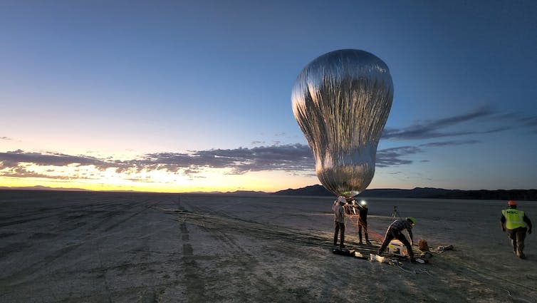 Large silver balloon being launched in the desert.