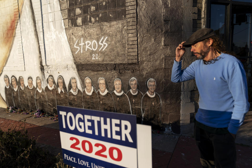 Artist Edward Stross stands next the mural he painted to honor the 13 nuns who died at a local convent from COVID-19, at his studio in Roseville, Mich., Saturday, Oct. 31, 2020. As the coronavirus crisis surges to more than nine million infections and 230,000 dead, the election for many is a referendum on how Trump has handled the pandemic. In the final days of the campaign, he has continued to downplay the toll it has taken, and many of his supporters say they find no fault in his response. (AP Photo/David Goldman)