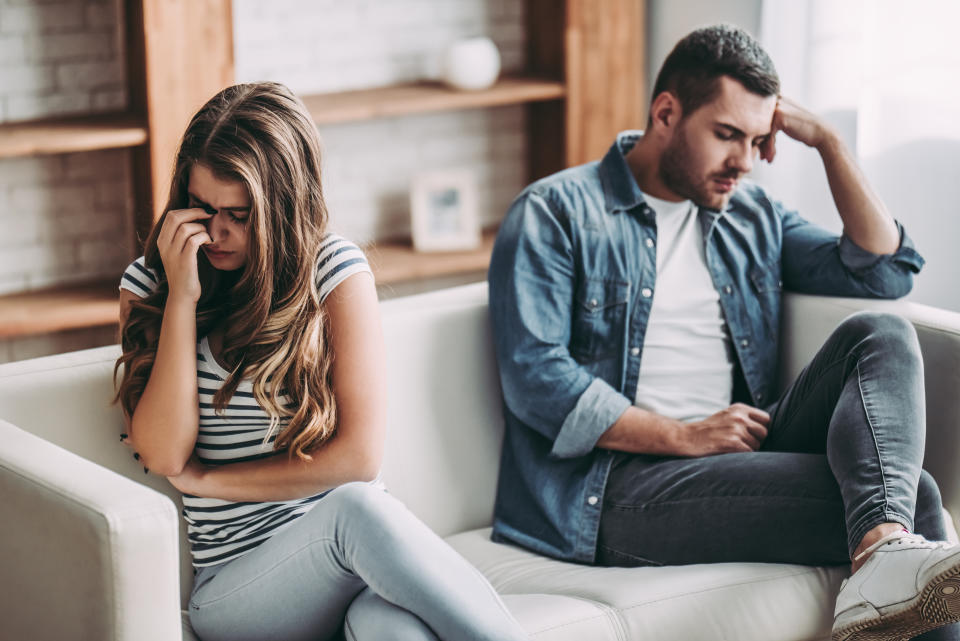 Upset couple at home. Handsome man and beautiful young woman are having quarrel. Sitting on sofa together. Family problems.