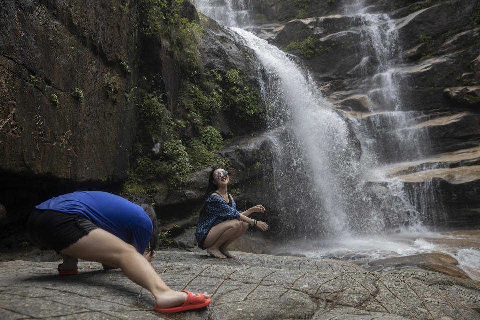 A woman poses for photos near a waterfall in Wuyishan in eastern China's Fujian province on Thursday, Aug. 15, 2019. (AP Photo/Ng Han Guan)