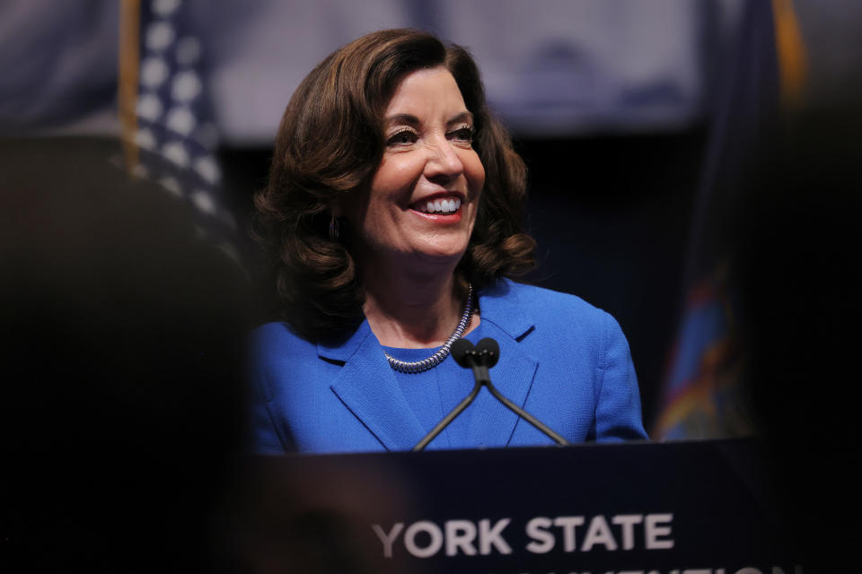 New York Gov. Kathy Hochul, in royal blue suit, smiles at a podium marked New York State.