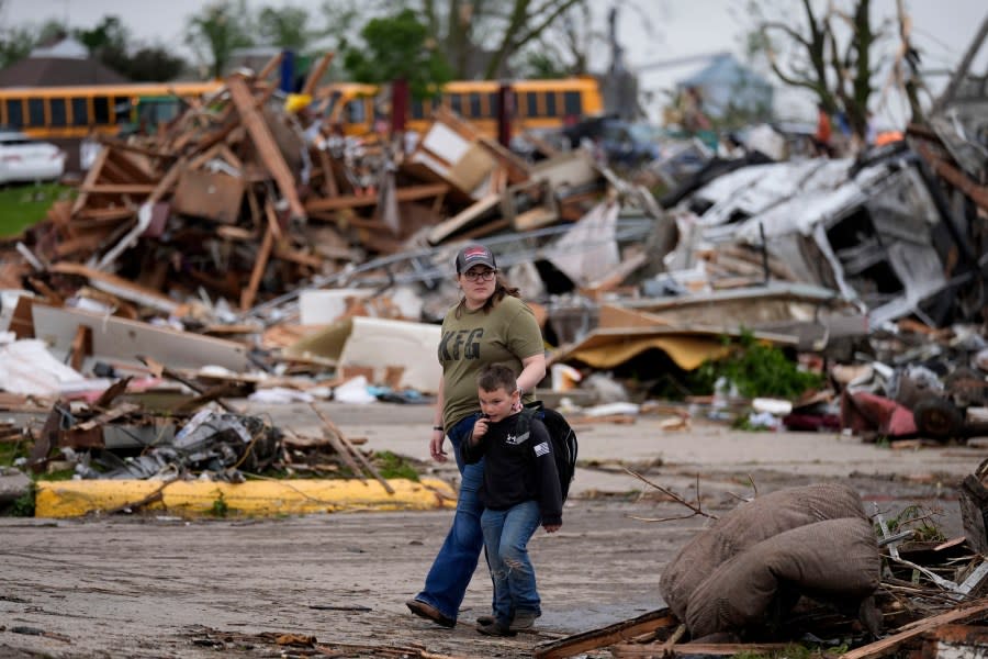 A woman and a child walk past damage after a tornado Tuesday, May 21, 2024, in Greenfield, Iowa. (AP Photo/Charlie Neibergall)