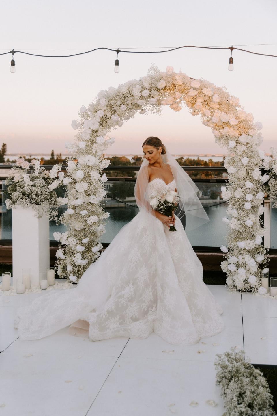 A bride stands in front of a floral arch in her wedding dress.