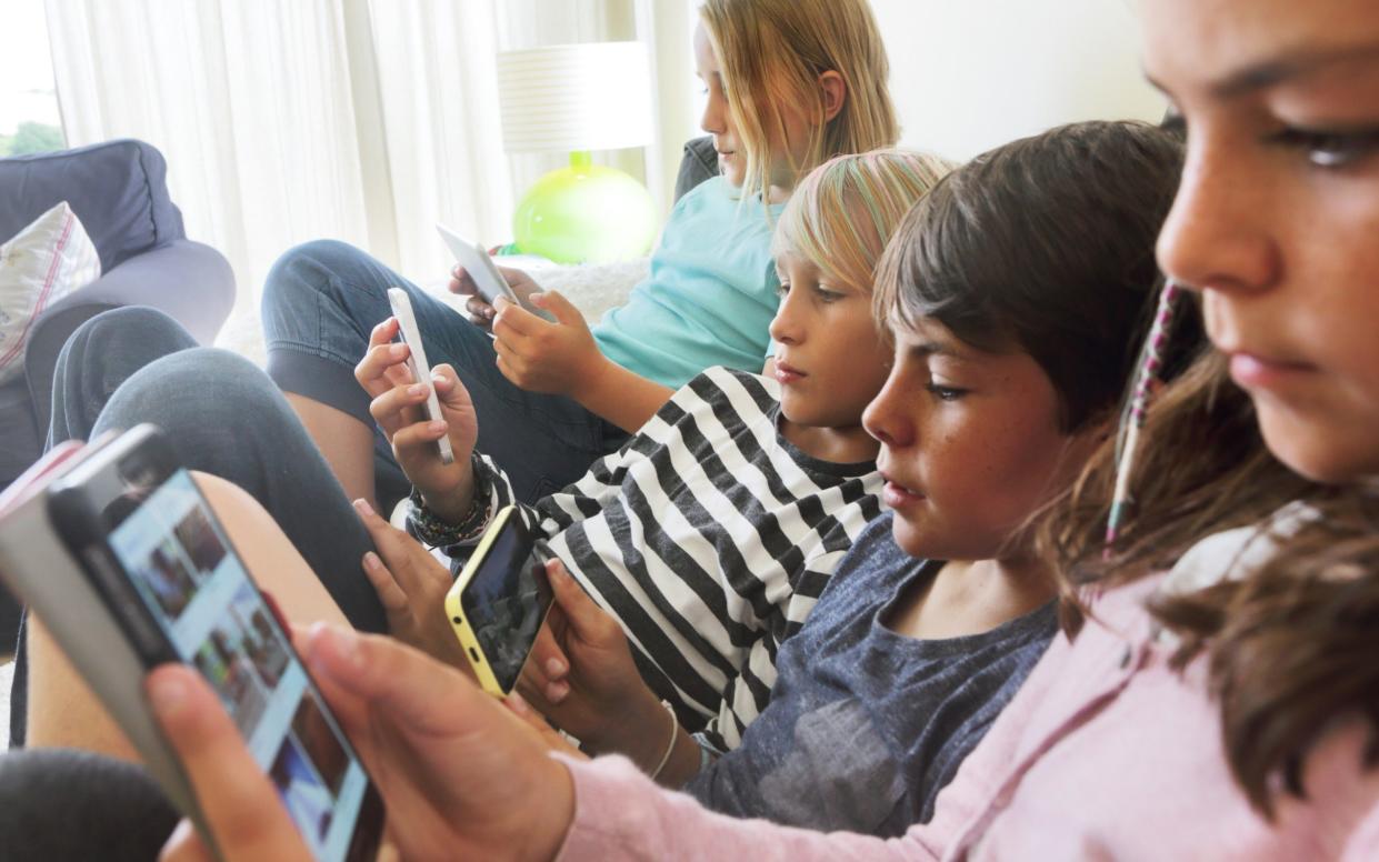 Four children on a sofa, looking at smartphones