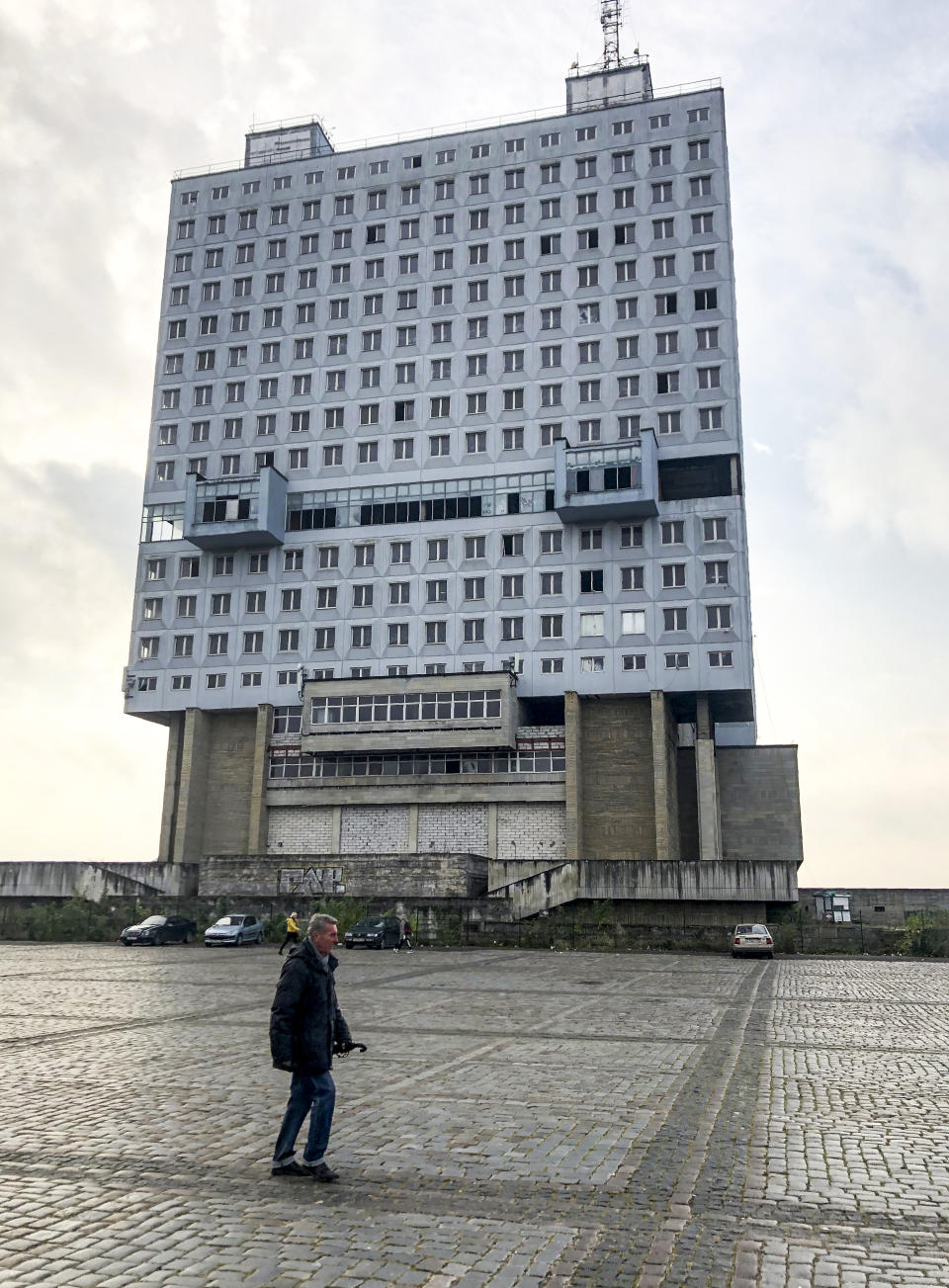 A man walks past the never-occupied building in Kaliningrad, Russia, Thursday, Oct. 29, 2020. The hulking never-occupied building sardonically likened to a robot's head that has loomed over the city of Kaliningrad for decades is to be demolished next year, the region's governor says. The 21-story House of Soviets was left unfinished when funding ran out in 1985 amid the Soviet Union's economic struggles and later was assessed to be structurally unsound. (AP Photo/James Heintz)