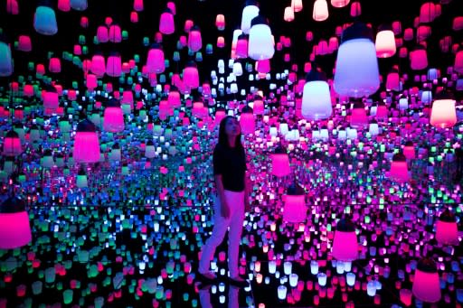 A member of the teamLab collective walks through a digital installation room in Tokyo featuring hanging lamps that light up as the visitor nears