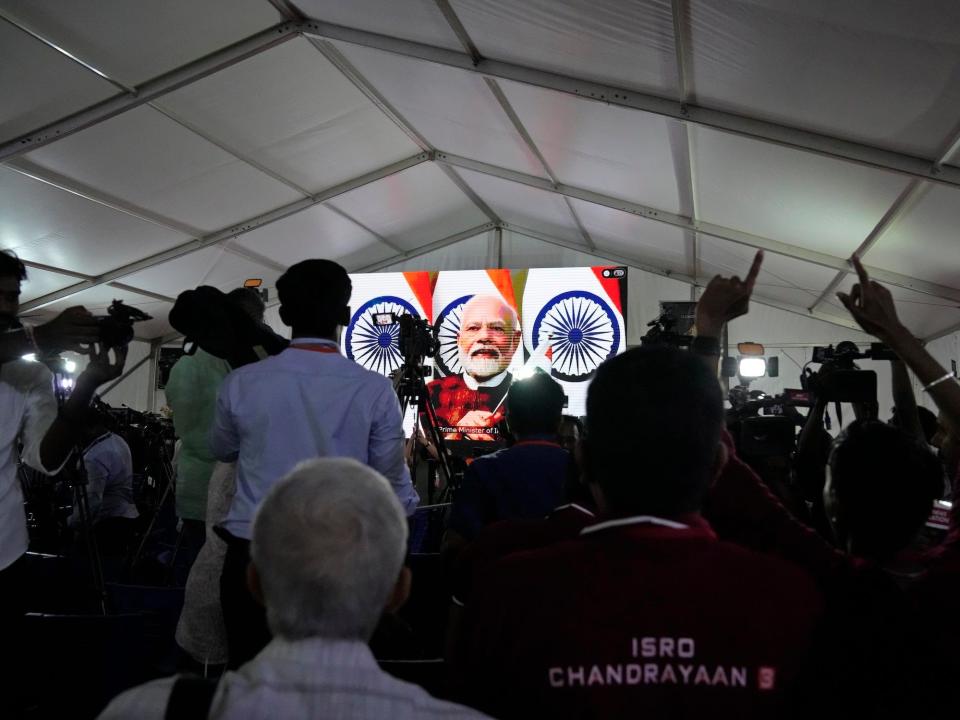 room full of men watches narendra modi on a screen under a white ceiling